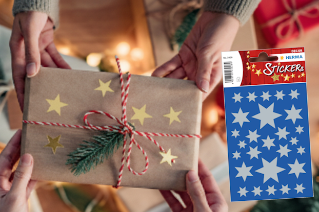 Geschenkverpackung mit goldenen HERMA Sternen, umgeben von Weihnachtsdekoration und zwei Rollen Geschenkpapier in Rot und Blau.