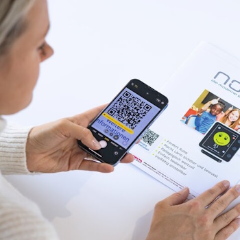 Eine Person scannt mit einem Smartphone einen QR-Code auf einem Informationsblatt mit QR-Code Etikett, das Details zu einem Produkt enthält.