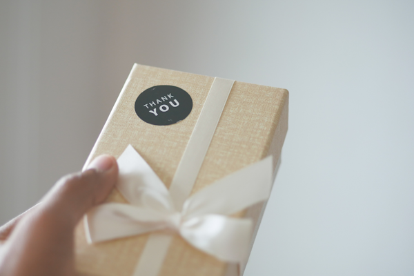 Eine Person hält ein Geschenk mit einem "Danke"-Aufkleber von HERMA und einer weißen Schleife in der Hand.