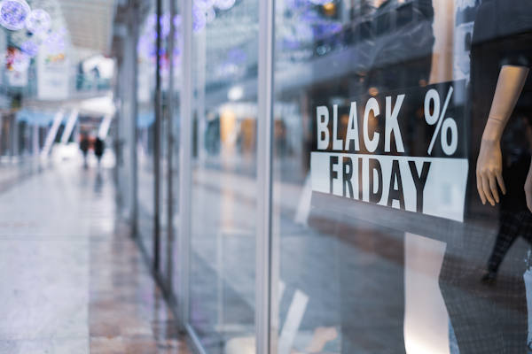 Schaufenster mit einem "BLACK FRIDAY" Schild, das Rabatte ankündigt. Im Hintergrund sind verschwommene Passanten und eine moderne Einkaufsumgebung zu sehen.