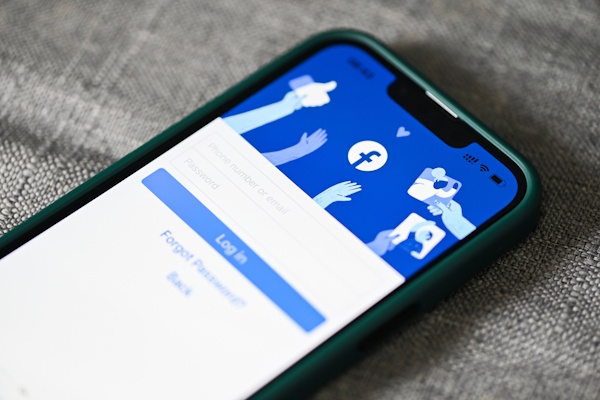 Ein Smartphone zeigt die Anmeldeseite von Facebook mit einem blauen Hintergrund und Symbolen für Interaktionen.