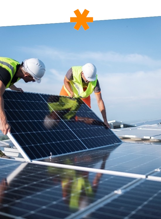 Zwei Arbeiter installieren Solarpanels auf einem Dach, tragen Sicherheitshelme und reflektierende Westen.