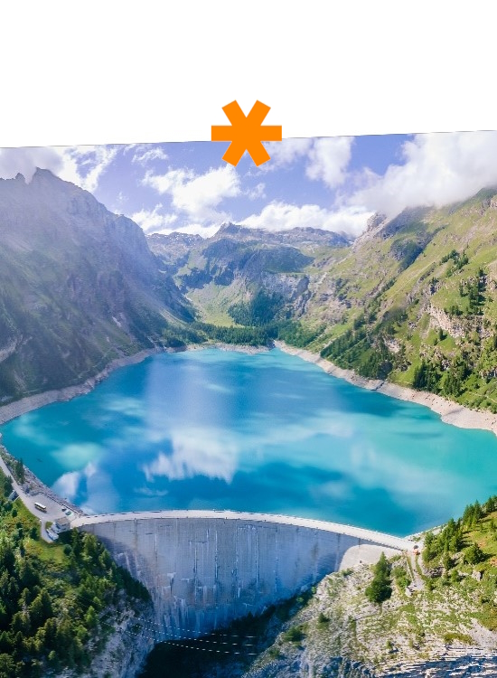 Ein klarer Stausee umgeben von Bergen und Wäldern, mit einer Betonmauer im Vordergrund, die das Wasser staut.