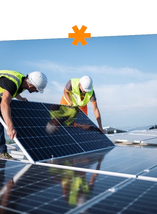 Arbeiter installieren Solarpanels auf einem Dach, tragen Sicherheitshelme und Warnwesten. Der Himmel ist klar und blau.