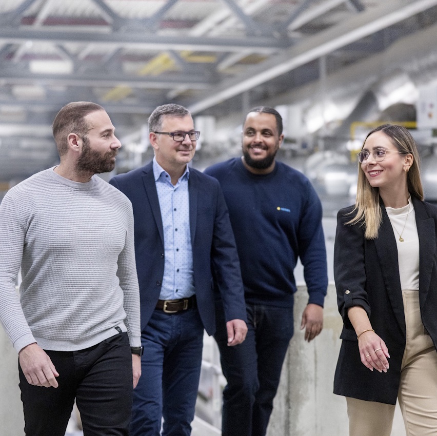 Vier Personen gehen in einem modernen Innenraum, lächelnd und in formeller Kleidung, während sie miteinander sprechen.