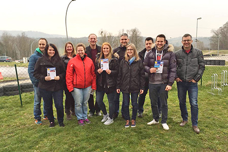 Eine Gruppe von zehn Personen steht auf einer Wiese, hält Broschüren in den Händen und posiert für ein Foto. Sie tragen verschiedene Winterjacken.