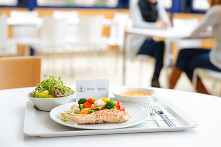 Ein Tablett mit gegrilltem Lachs, Gemüse, Salat und einer Schüssel Suppe, daneben eine Menükarte.