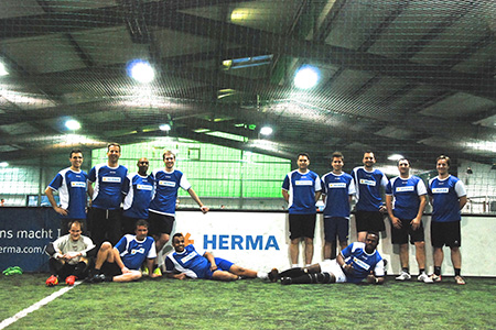 Eine Gruppe von Fußballspielern in blauen Trikots posiert auf einem Kunstrasenfeld in einer Sporthalle.