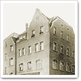 Historisches Gebäude mit Ziegelfassade und Giebeldach, mehrere Fenster sichtbar, in sepiafarbener Darstellung.