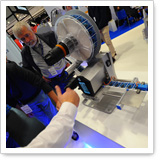 Eine Person demonstriert ein technisches Gerät mit einem großen, runden Teil und einem Handgriff auf einer Messe.