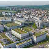 Luftaufnahme eines modernen Stadtgebiets mit mehreren Gebäuden und begrünten Dächern, umgeben von einer ländlichen Landschaft.