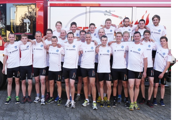 Eine Gruppe von 22 Männern in weißen T-Shirts und kurzen Hosen steht vor einem Feuerwehrauto und posiert gemeinsam für ein Gruppenfoto.