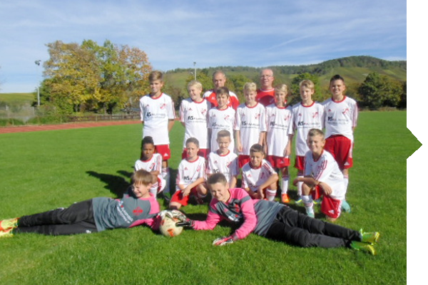 Eine Jugendfußballmannschaft posiert auf einem Rasenplatz, gekleidet in weiße und rote Trikots, mit einem Ball im Vordergrund.