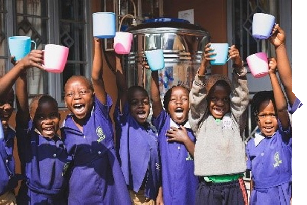 Eine Gruppe von Kindern in blauen Schuluniformen hebt fröhlich bunte Tassen in die Luft, während sie vor einem Wasserbehälter stehen.