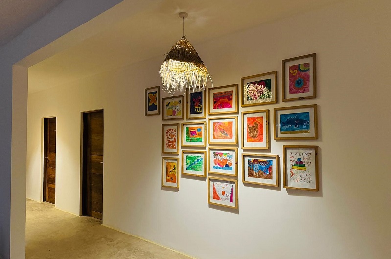 Ein Flur mit einer Wand, die mit gerahmten Kinderzeichnungen dekoriert ist. Zwei Türen sind im Hintergrund sichtbar. Eine hängende Lampe ist ebenfalls zu sehen.