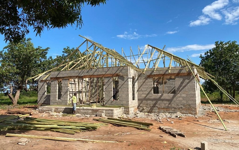 Ein unvollendetes Haus mit einer Holzrahmenkonstruktion für das Dach, umgeben von Bäumen und Baustellenmaterialien.