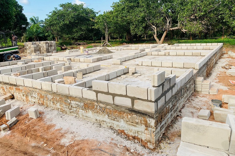 Ein Baugrundstück mit einer teilweise errichteten Mauer aus Betonsteinen, umgeben von Bäumen und unbefestigtem Boden.