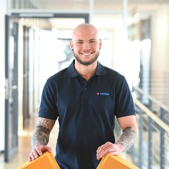 Ein Mann mit Glatze trägt ein dunkelblaues Polo-Shirt und hält zwei orangefarbene Objekte in den Händen.