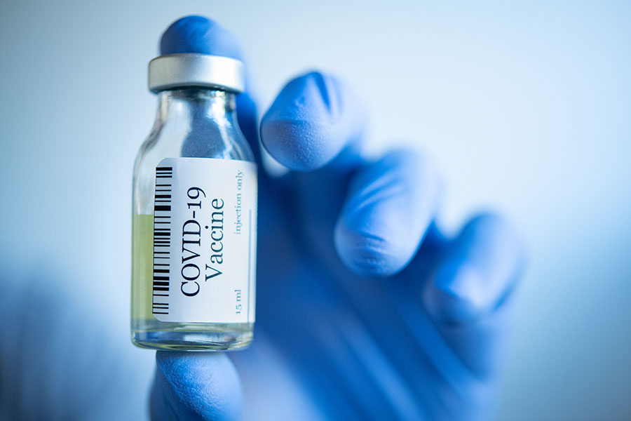 Eine Hand mit blauen Handschuhen hält eine Glasflasche mit der Aufschrift "COVID-19 Vaccine".