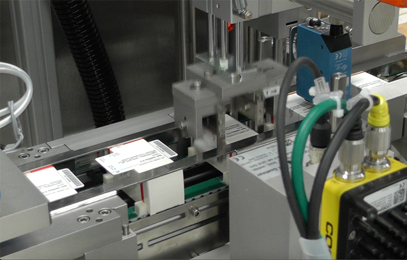 Automatisierte Maschinenkomponenten, die Etiketten auf Produkte anwenden. Sichtbare Etiketten mit Text auf einem Förderband.
