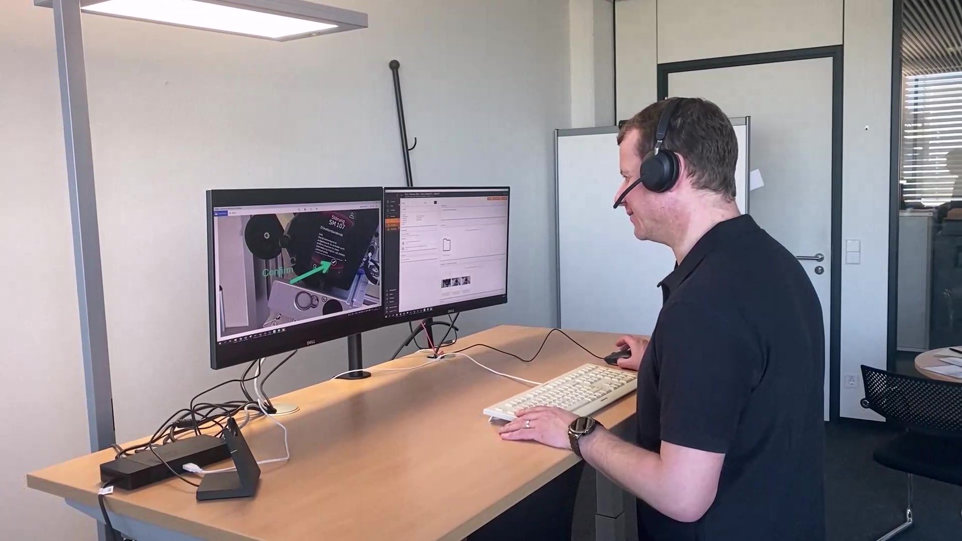 Ein Mann sitzt an einem Schreibtisch mit zwei Monitoren, trägt ein Headset und arbeitet an einem Computer.