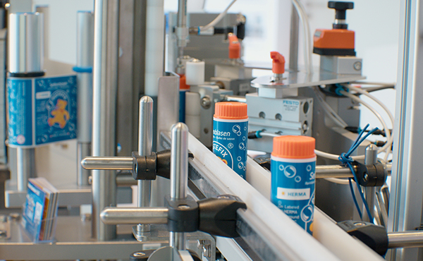 Maschinen zur Abfüllung von Flaschen mit orangefarbenen Deckeln auf einem Förderband in einer Produktionsumgebung.