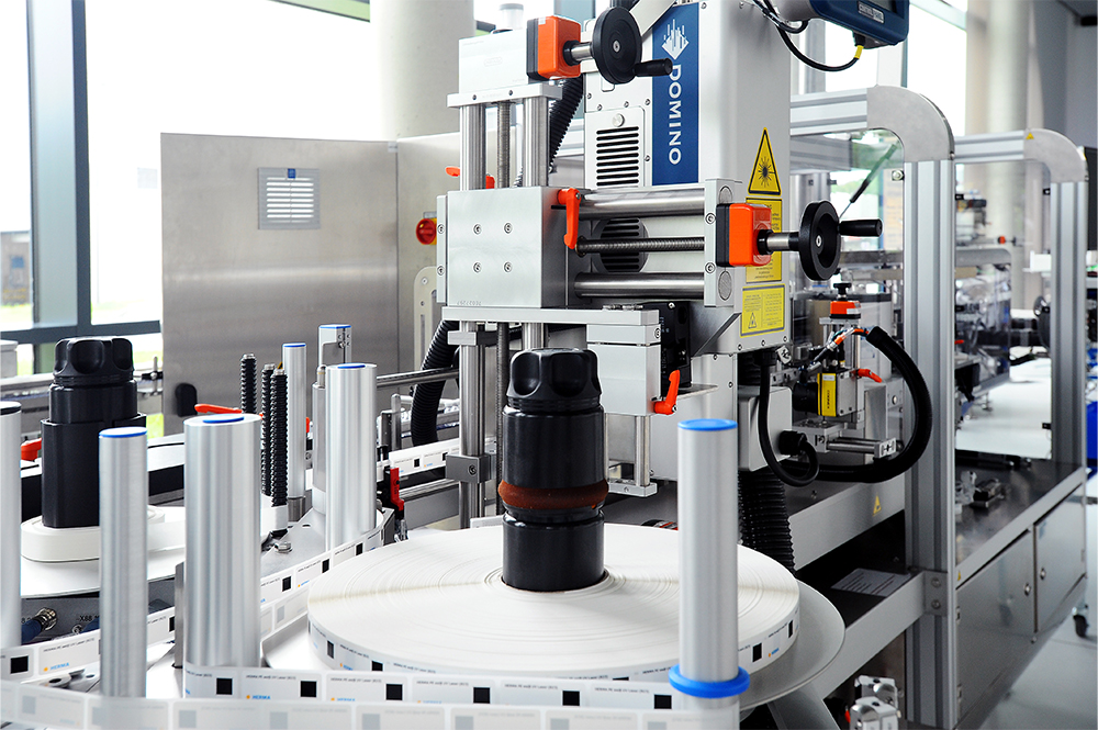 Eine automatisierte Verpackungsmaschine mit Flaschen auf einem Förderband, ausgestattet mit Etikettier- und Drucksystemen.