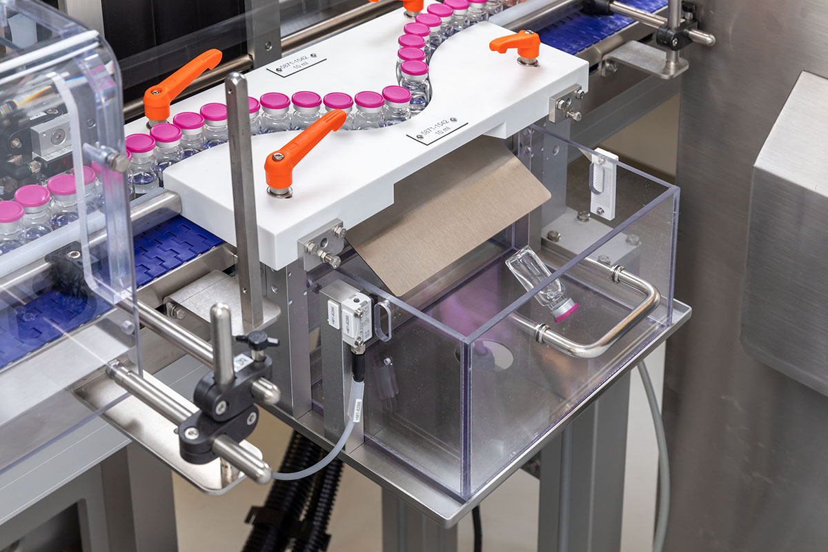 Automatisierte Abfüllanlage mit Flaschen auf einem Förderband und einem Behälter zur Aufnahme von Verpackungsmaterial.