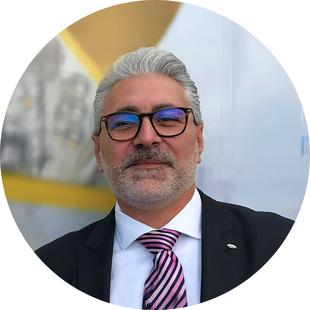 Mann mit grauen Haaren und Brille, trägt einen Anzug mit gestreifter Krawatte. Hintergrund unscharf und hell.