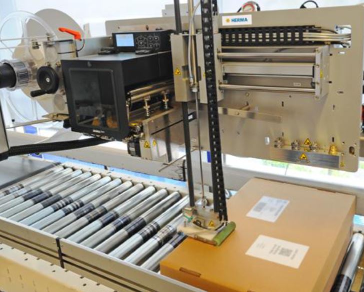 Automatisierte Etikettieranlage mit einem Karton auf einem Förderband, ausgestattet mit Druck- und Etikettiermechanismen.