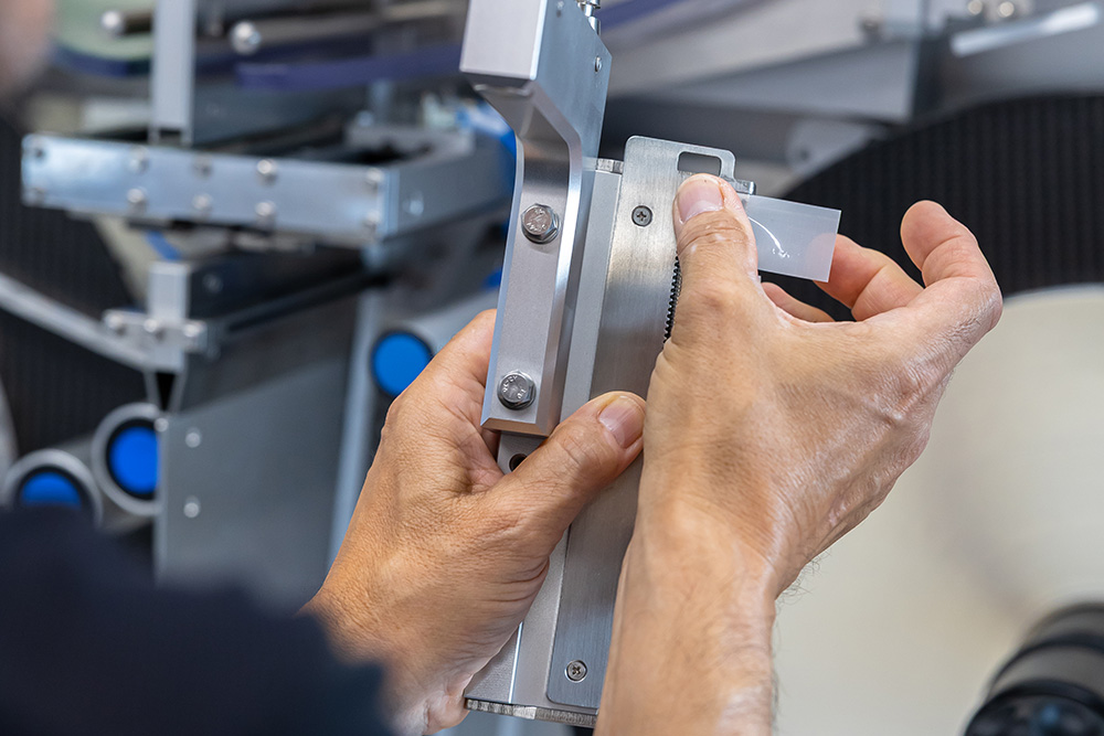 Eine Person justiert ein präzises Messinstrument mit beiden Händen, während sie an einer technischen Maschine arbeitet.