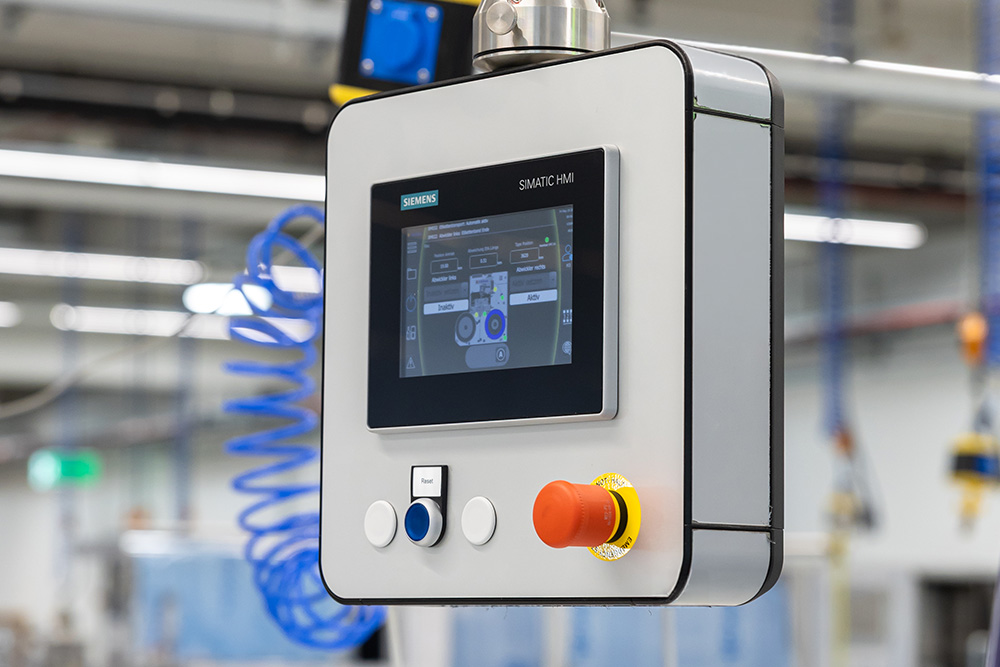 Bedienfeld mit Touchscreen und Steuerknöpfen, das zur Steuerung von Maschinen in einer industriellen Umgebung verwendet wird.