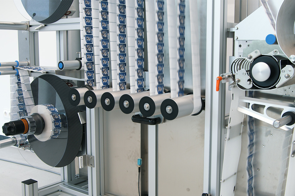 Maschine zur Verarbeitung von Bändern, mit mehreren Rollen und einem mechanischen System zur Anordnung der Materialien.