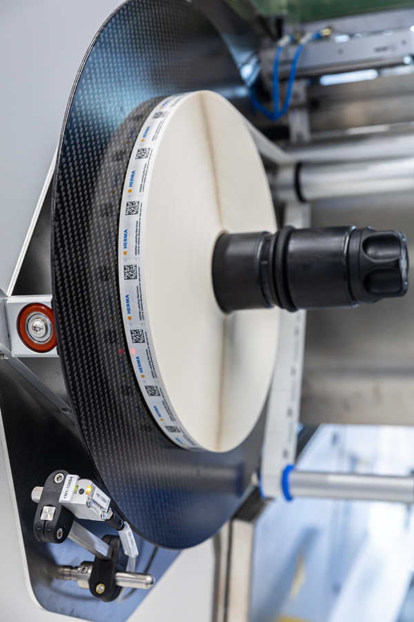 Eine große, runde Rolle aus Carbon mit einem zentralen schwarzen Halter, umgeben von technischen Komponenten und Sensoren.