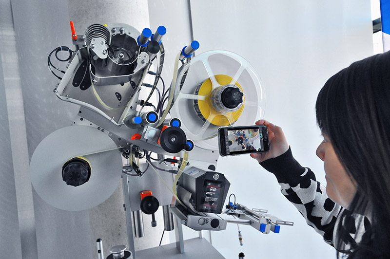 Eine Person fotografiert ein mechanisches Gerät mit Filmrollen und verschiedenen Bedienelementen.