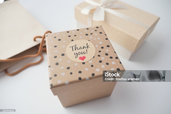 Geschenkbox aus Kraftpapier mit einem "Danke!"-Aufkleber, umgeben von weiteren Geschenken und einer Tasche.