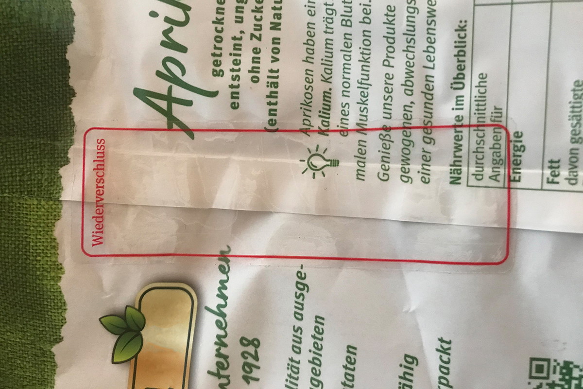 Verschlussetiketten: transparentes Wiederverschlussetikett, bedruckt mit farbigem Rahmen und Text Widerverschluss, auf Schlauchbeutelverpackung mit Aprikosen