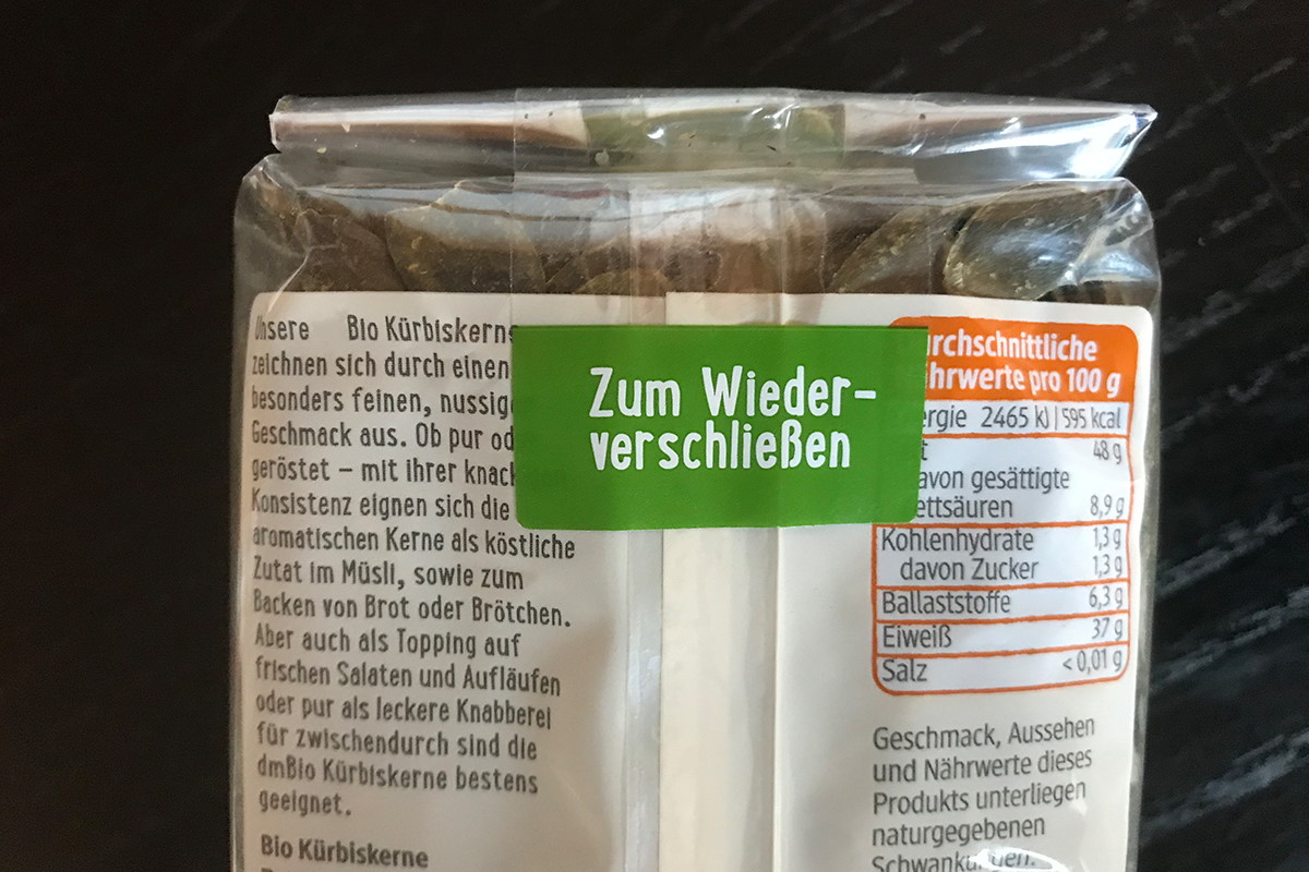 Verschlussetiketten: transparentes Wiederverschlussetikett mit farbig bedruckter Anfasslasche, auf Schlauchbeutelverpackung mit Kürbiskernen