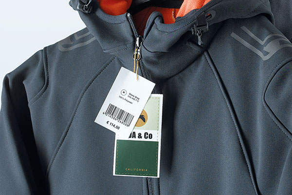 Farbig bedruckte Anhängeetiketten mit Preis- und Warenkennzeichnung, an grauer Softshell-Jacke
