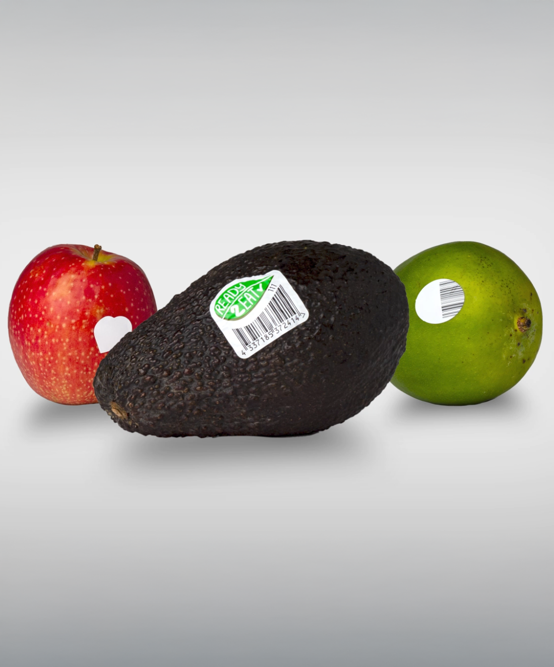 Ein schwarzes Avocado mit einem Preisschild, flankiert von einem roten Apfel und einer grünen Limette.
