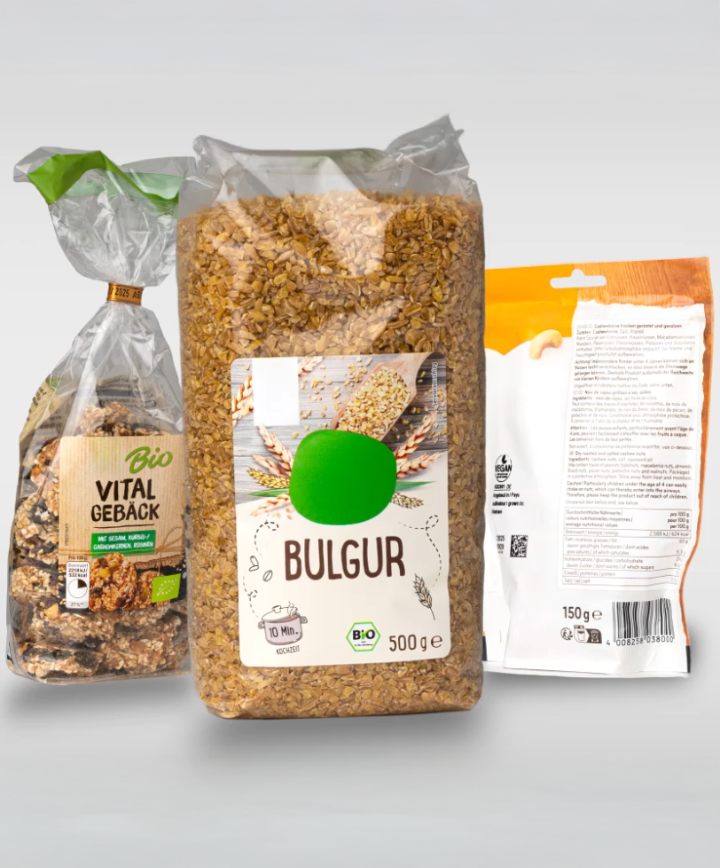 Drei Verpackungen von Lebensmitteln: eine mit Bulgur, eine mit vitalem Gebäck und eine weitere mit unleserlichem Text auf der Rückseite.