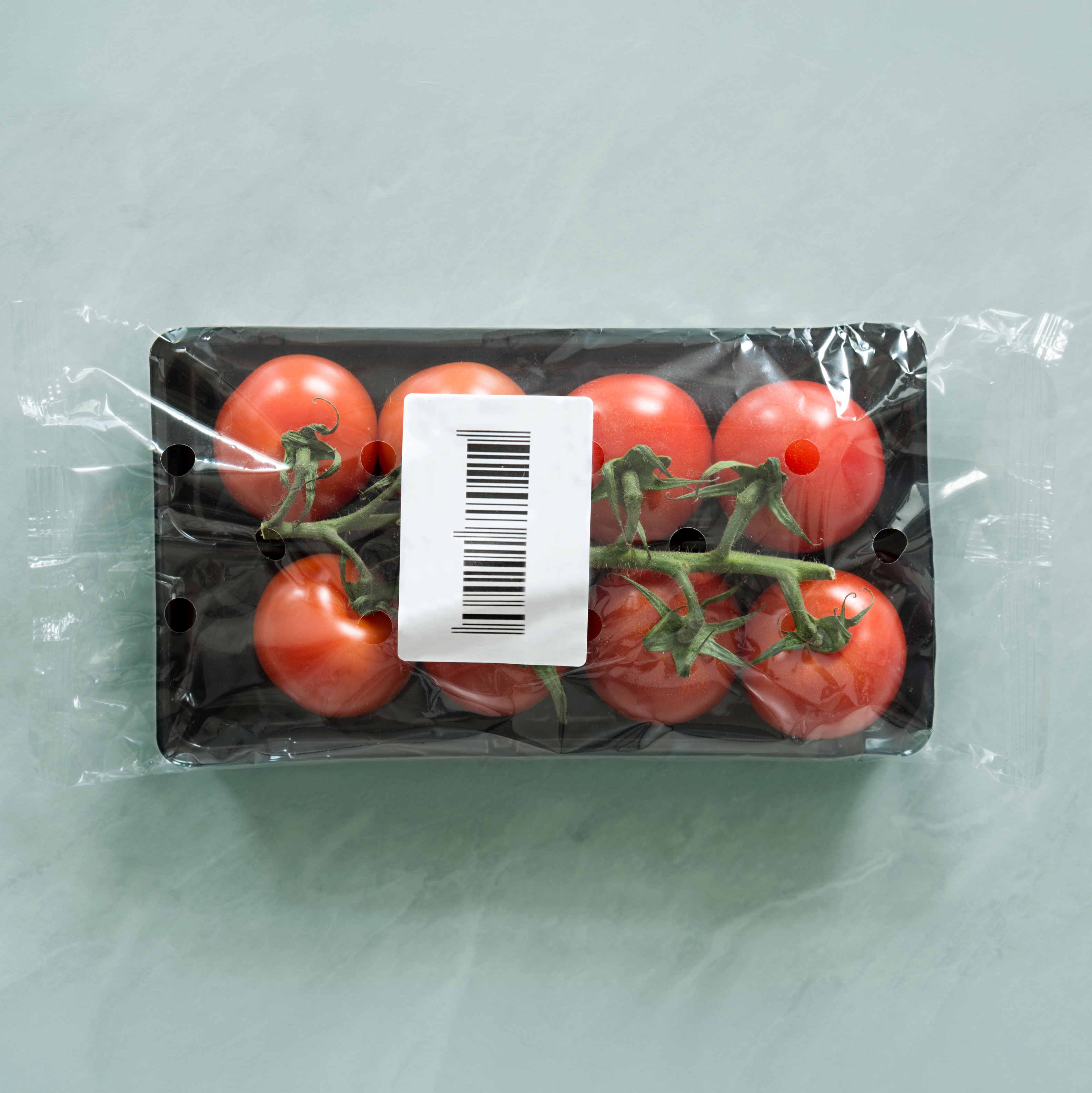 Sechs rote Tomaten in einer schwarzen Verpackung mit einem Barcode. Die Tomaten sind am Stängel befestigt.