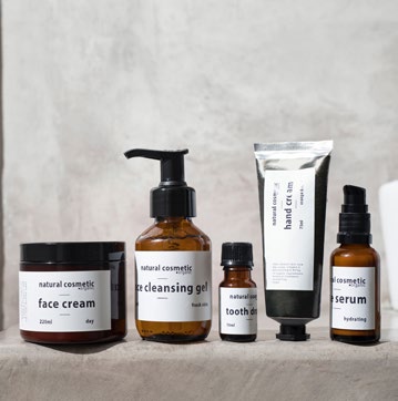 Eine Reihe von Naturkosmetikprodukten, darunter Gesichtscreme, Reinigungsgel, Zahnöl, Handcreme und Serum, auf einem neutralen Hintergrund.