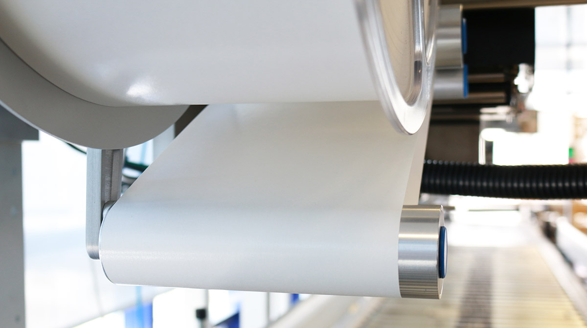 Eine Rolle mit weißem Papier, die von einer Maschine abgewickelt wird, mit einem Fokus auf die Walze und die Papierkante.