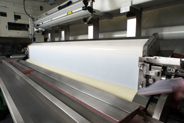Eine industrielle Maschine, die eine lange, flache Teigbahn verarbeitet, mit einem Fokus auf den Produktionsprozess.