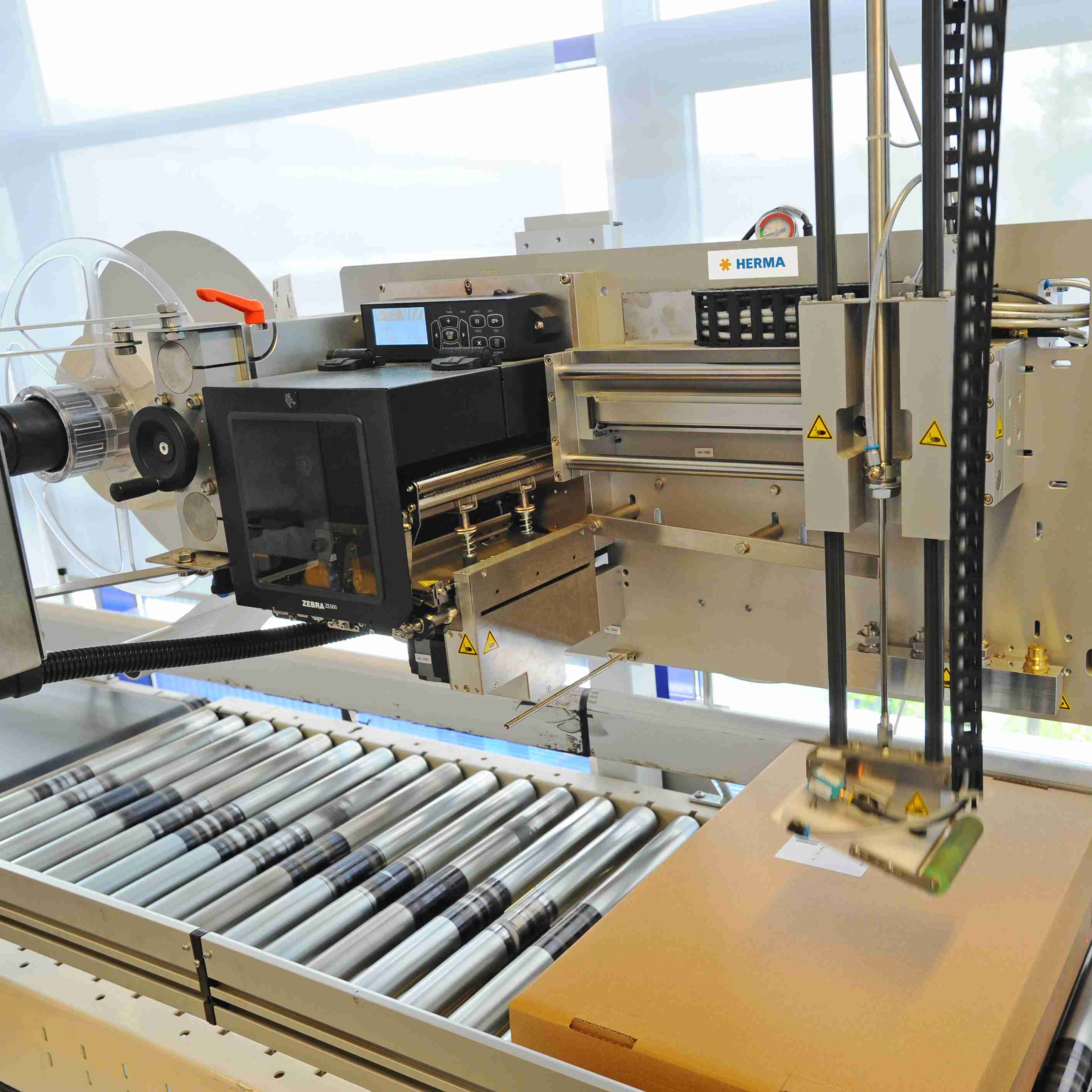 Automatisierte Etikettiermaschine mit Förderband und Steuerungseinheit, die Kartons etikettiert.