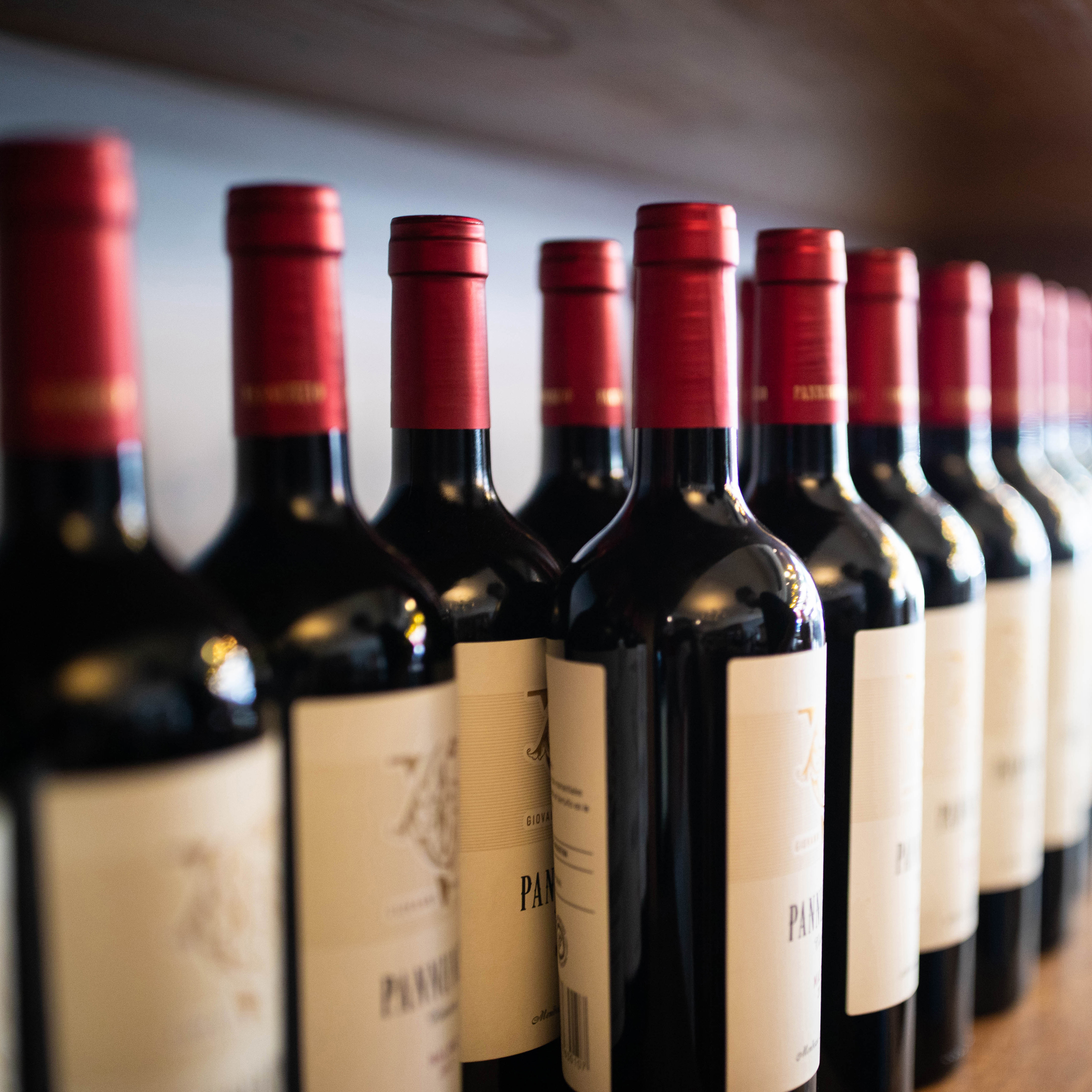 Reihe von Rotweinflaschen mit roten Kappen, etikettiert und auf einem Regal angeordnet.