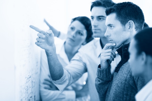 Eine Gruppe von vier Personen betrachtet aufmerksam eine Wand mit Diagrammen und diskutiert darüber.