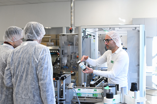 Ein Mitarbeiter erklärt einer Gruppe von Personen in Schutzkleidung die Verwendung eines Behälters in einer Produktionsumgebung.