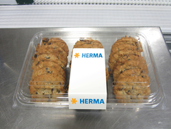 Ein Behälter mit mehreren Schokoladenkeksen, in der Mitte mit einem Etikett, das "HERMA" zeigt.